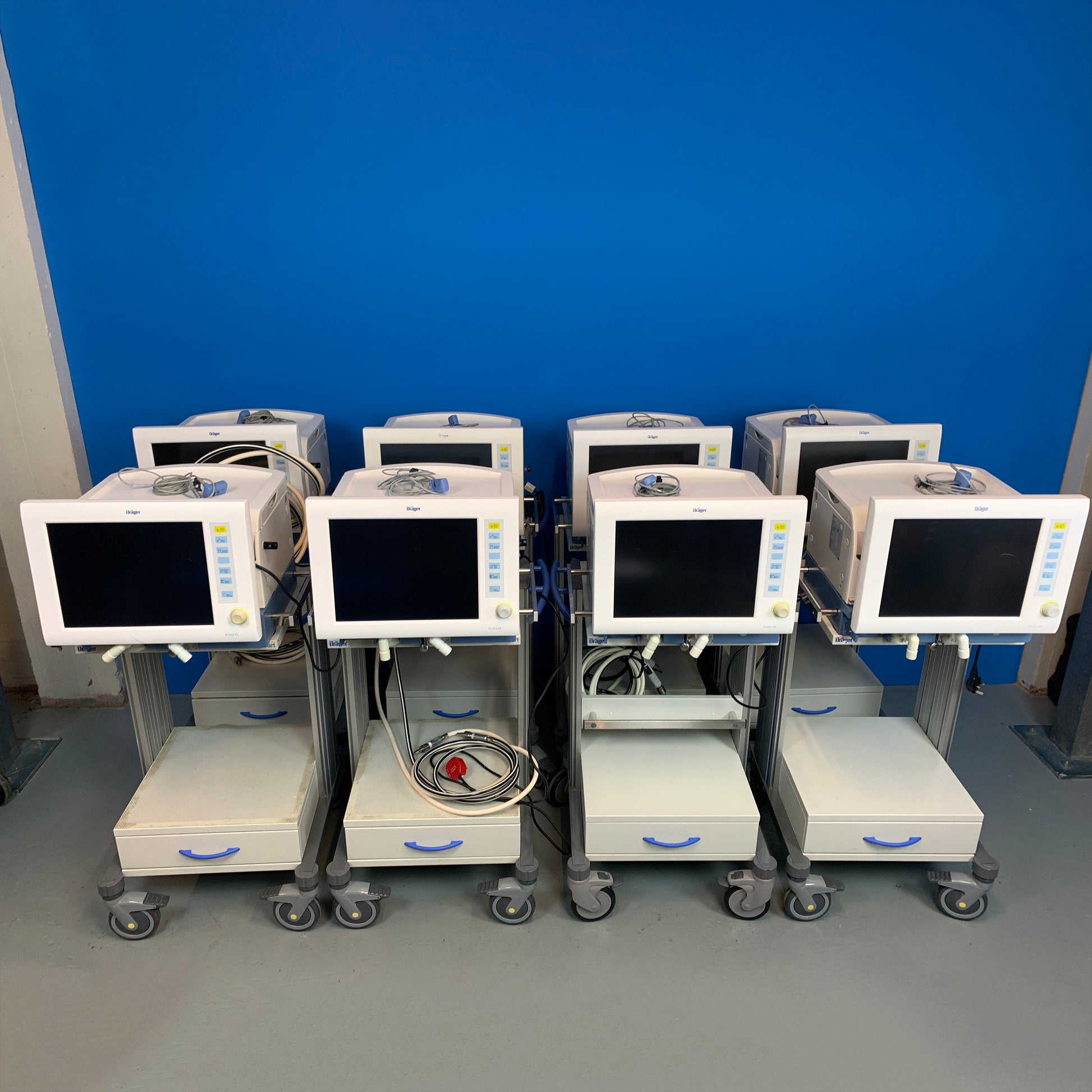 Quantity 8 Evita XL ICU Ventilators on cart lined up against the blue background